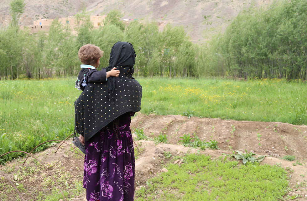 Une femme avec un enfant dans les bras regarde vers une montagne.