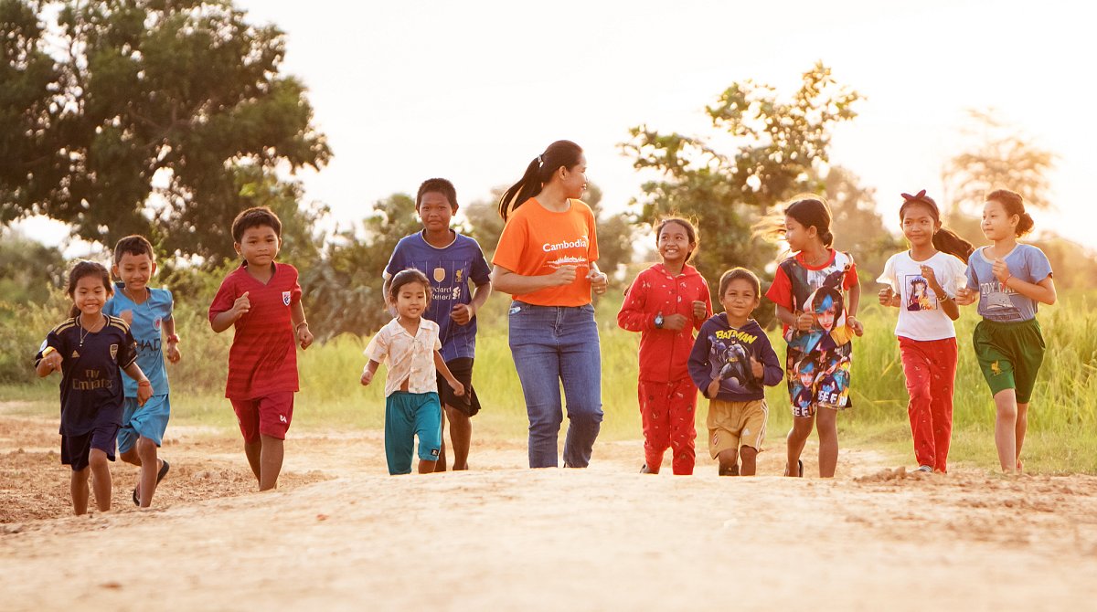 Kambodscha: Mädchen und Jungs halten sich mit einer World Vision-Mitarbeiterin draussen in der freien Natur auf.