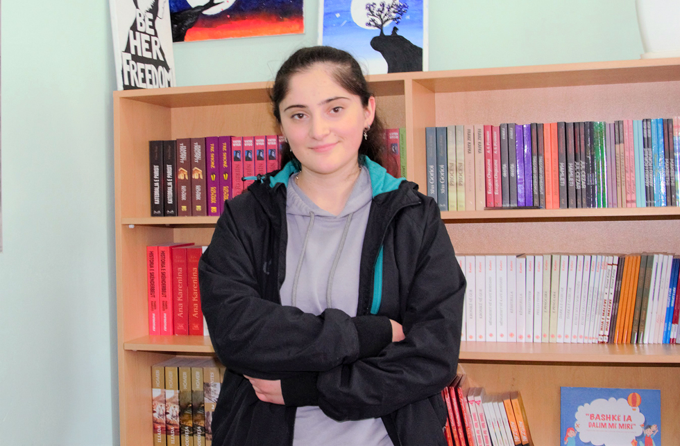 Albanien: Ein Mädchen steht vor einem Büchergestell