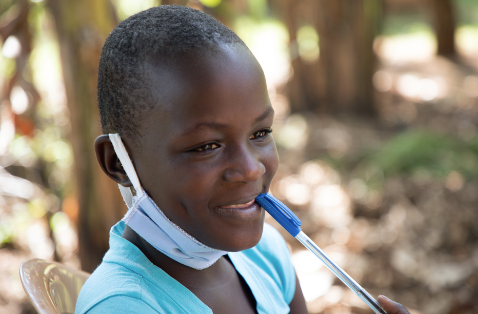 Ein Mädchen in Uganda hält einen Kugelschreiber an die Lippen