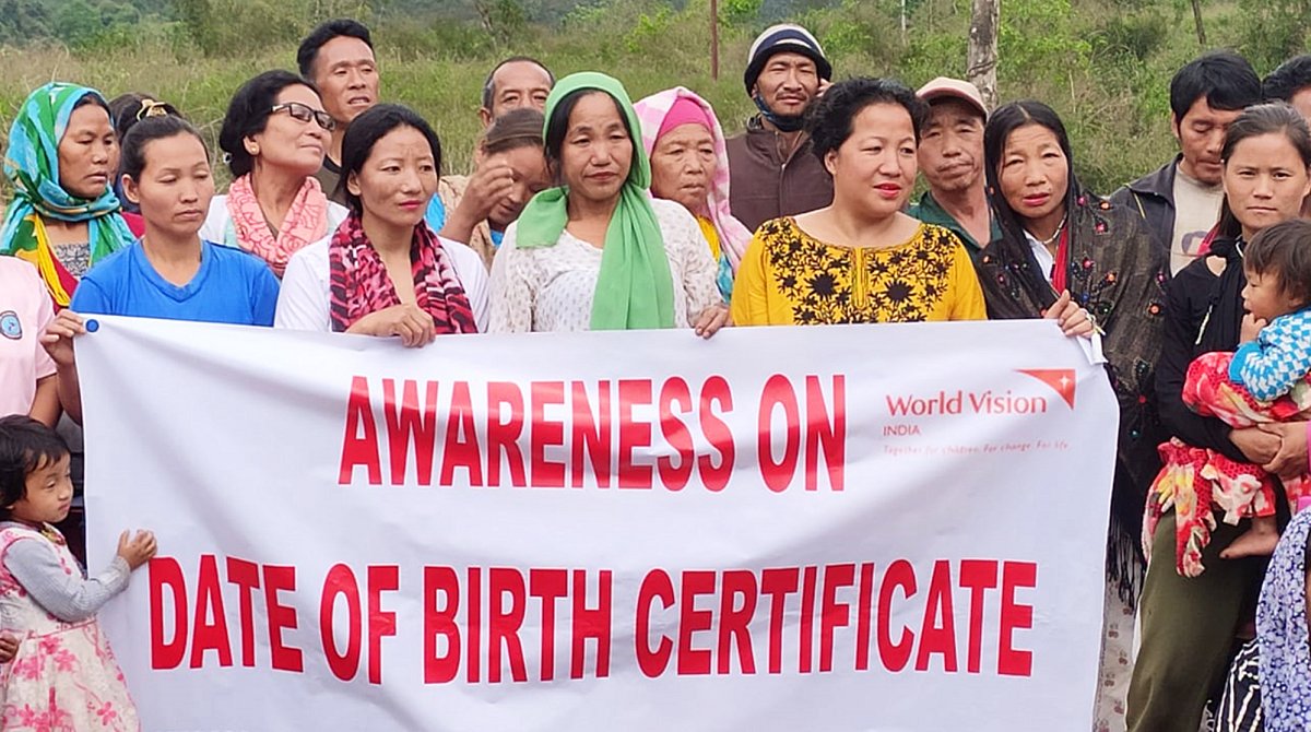 Indien: Frauen und Männer halten ein Plakat in den Händen, die an die Bedeutung von Geburtsurkunden erinnert