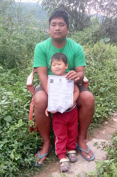 Indien: Vater und Tochter, der Vater hält eine Geburtsurkunde in den Händen.