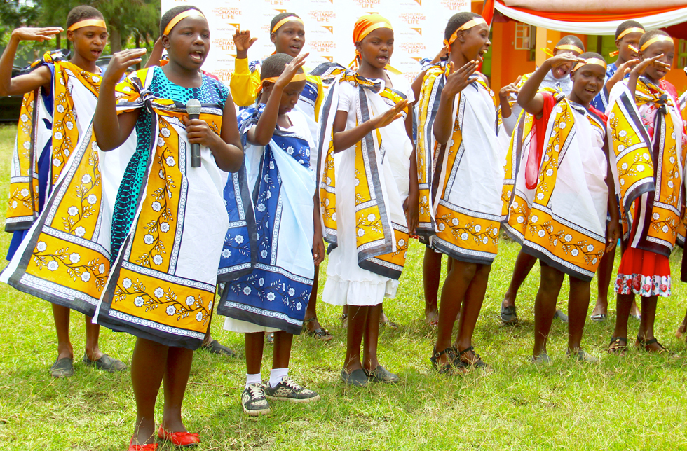 Mädchen in Kenia mit gemusterten Umhängen singen ein Lied.