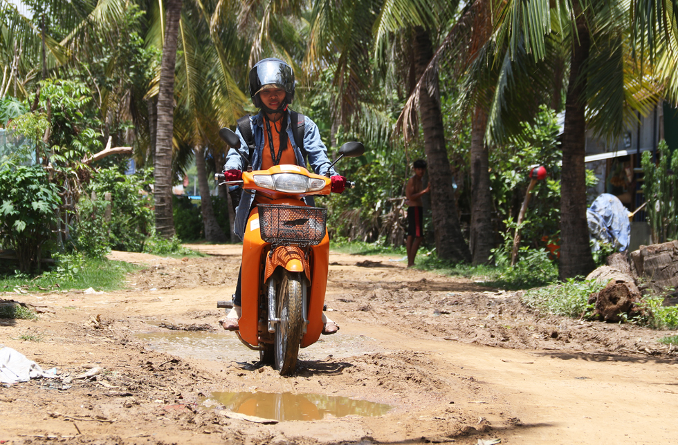 Un collaborateur de World Vision au Cambodge apporte des lettres aux enfants parrainés en mobylette sur une route de terre glissante et accidentée.