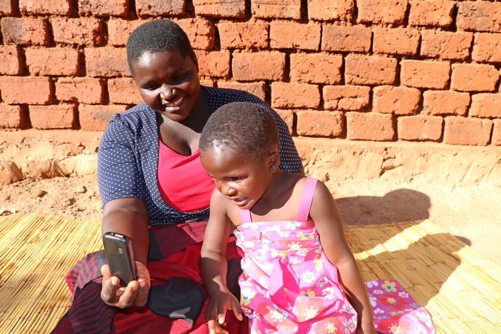 Au Zimbabwe, une femme montre l'écran de son téléphone portable à une petite fille