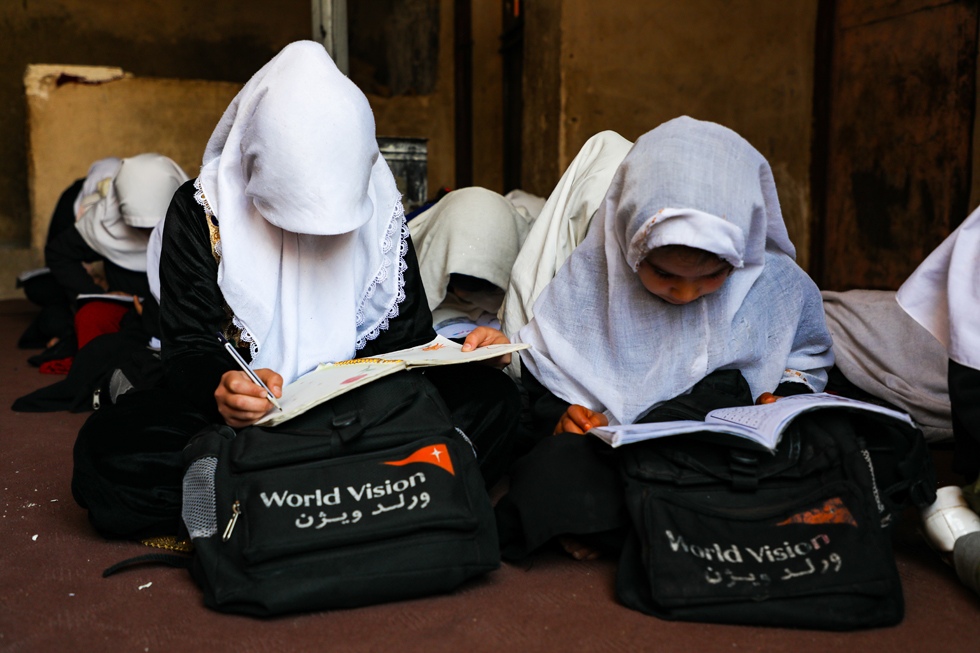 Afghanistan: Mädchen sitzen mit Schulheften und World Vision-Schultaschen auf dem Boden im Klassenzimmer.
