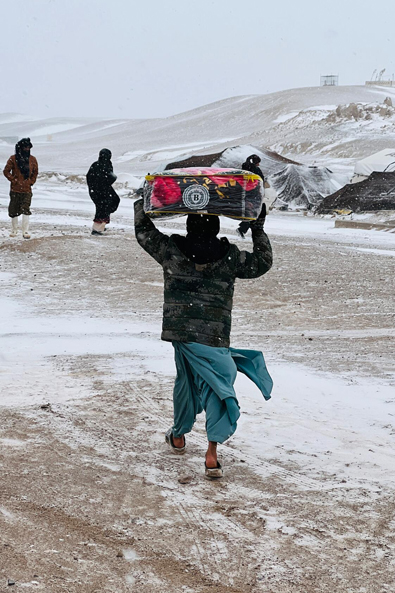 Afghanistan : un homme en sandales porte un paquet de couvertures à travers la tempête de neige.