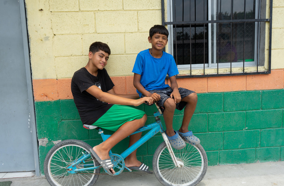 Honduras: Zwei Jungen sitzen zu zweit auf einem Kindervelo.