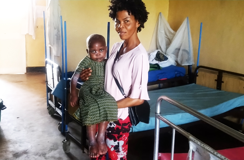 Demokratische Republik Kongo: Eine World Vision-Mitarbeiterin steht vor auf einem Spitalbett und hält ein Kind auf ihren Armen.