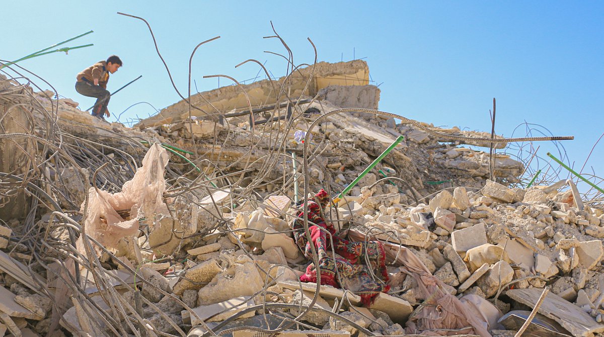 Ein Mensch steht vor einem in Trümmer gelegten Gebäude.
