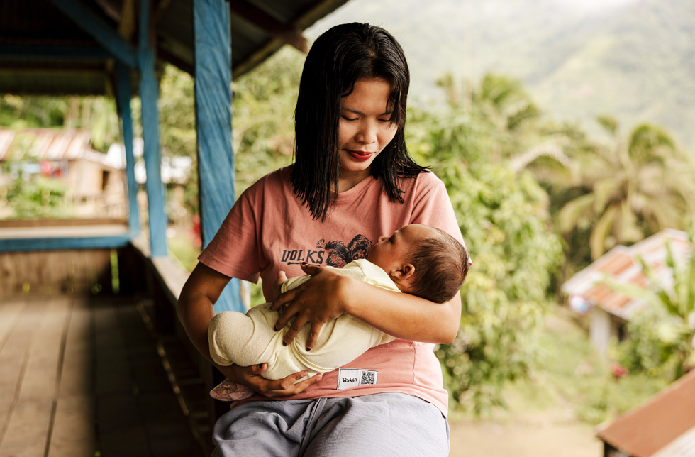 Indonesien: Junge Frau hält ihr Baby im Arm und lächelt.