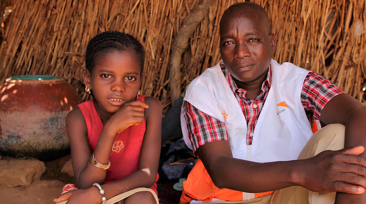 Mali : une fillette est assise à côté d'un collaborateur de World Vision.