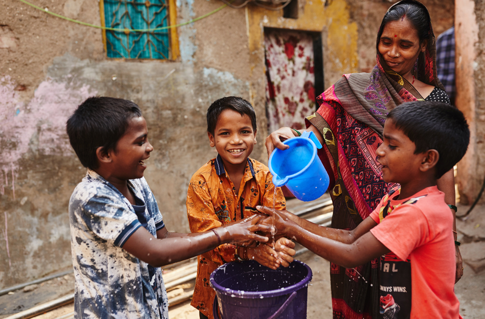 Inde : une femme verse de l'eau sur les mains de ses enfants avec un récipient en plastique.
