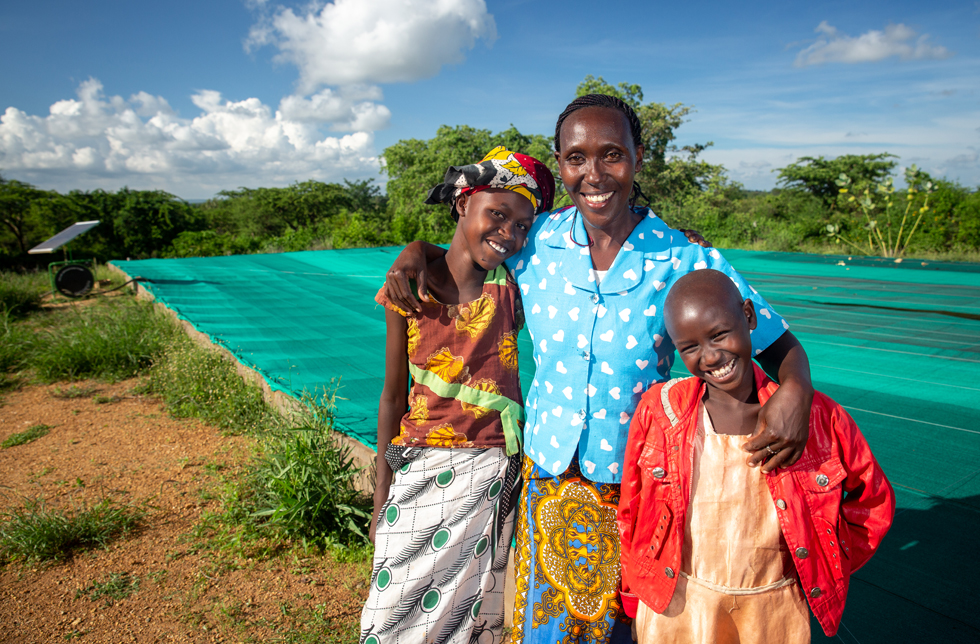 Kenya : une femme et deux filles se tiennent devant un champ recouvert d'un film plastique.