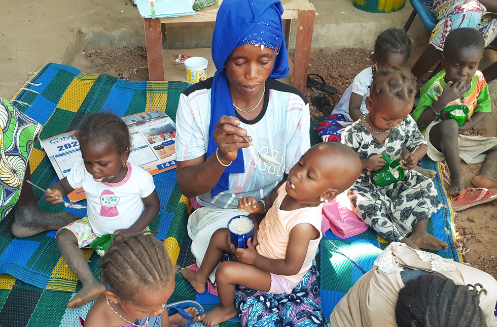 Mali: Eine Mutter ernährt ihr Kind mit dem Löffel. Um sie herum sitzen weitere Kinder und Mütter.