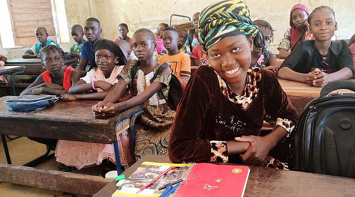 Mali: Ein Mädchen sitzt inmitten ihrer Mitschülerinnen und -schülern im Schulzimmer.