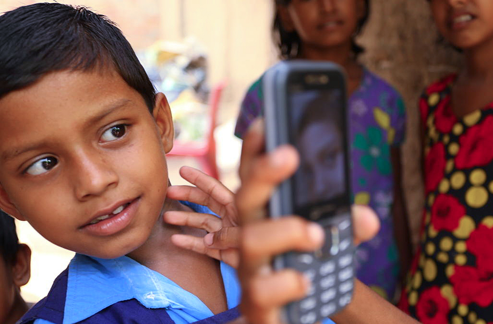 Ein Junge zeigt sein altes Mobiltelefon mit dem Bild einer Person.