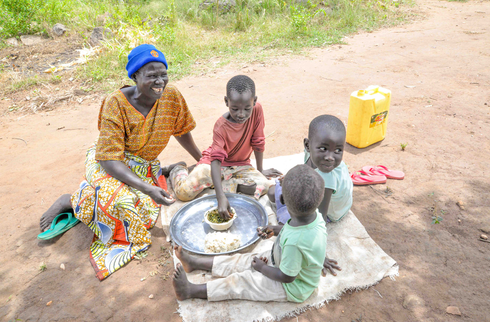 Uganda: Eine Mutter und ihre drei Kinder sitzen am Boden und essen von einem Teller.