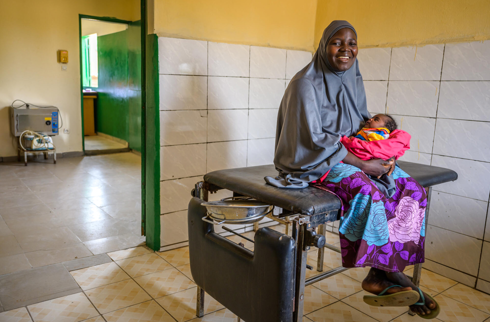 Niger: Eine junge Frau mit Neugeborenem im Arm sitzt in einem einfachen Gebärsaal in der Klinik.