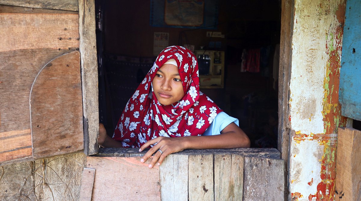 Philippinen: Ein Mädchen mit Kopftuch schaut aus dem Fenster einer einfachen Hütte.