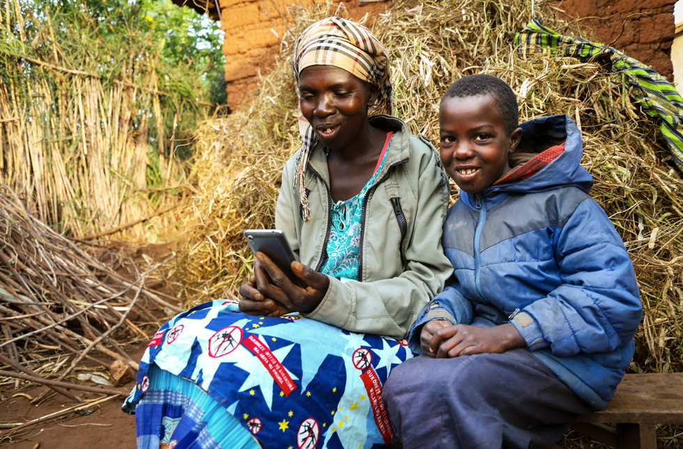 Mutter und Tochter sitzen mit einem Mobiltelefon vor ihrer Scheune in Ruanda.