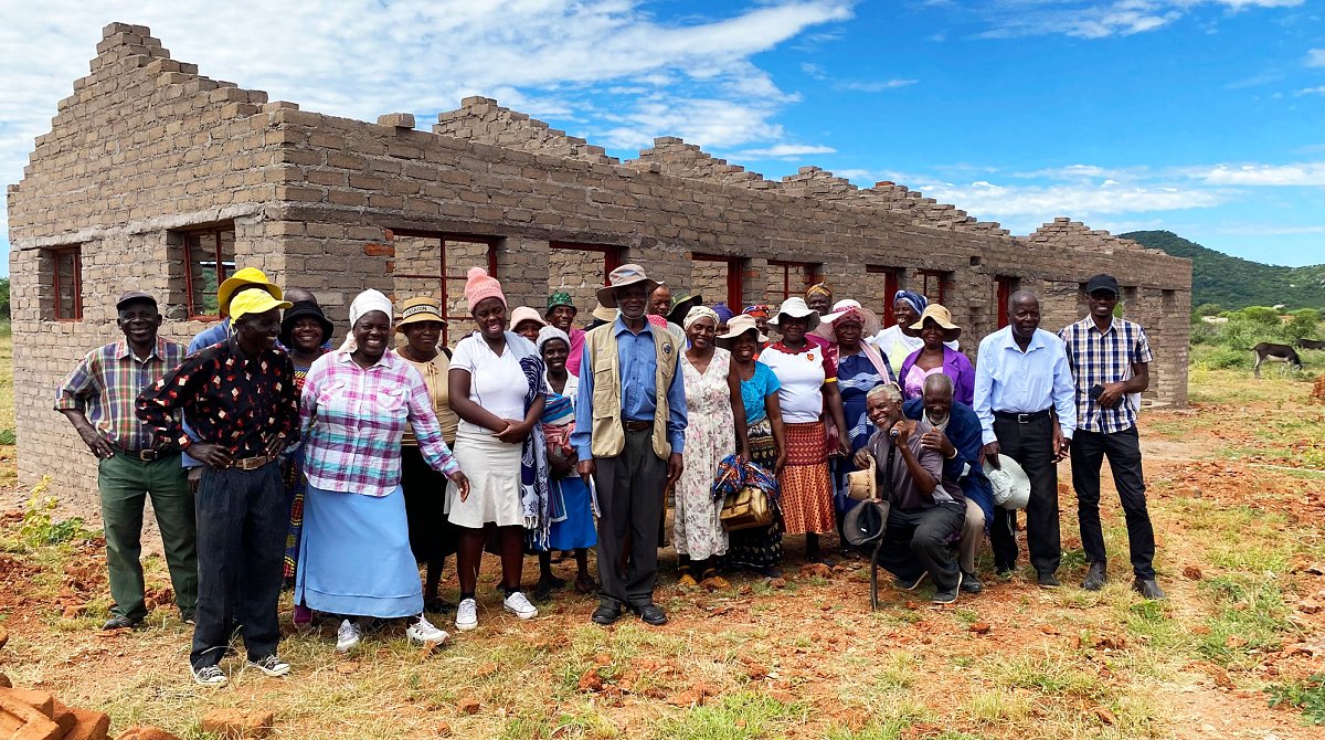Simbabwe: Eine Gruppe Menschen steht vor dem Rohbau eines Gebäudes aus Backsteinen.