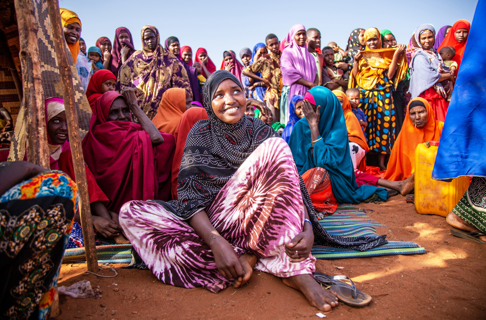 Eine junge Frau sitzt inmitten vieler Menschen lachend auf dem Boden im World Vision-Nothilfezentrum in Somalia.