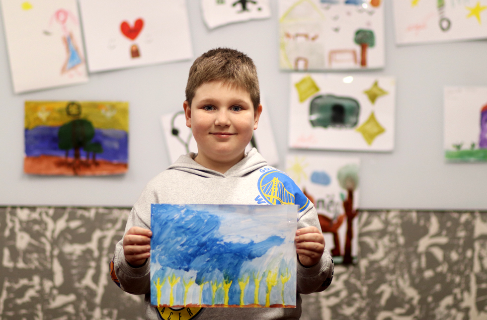 Ukraine: Ein Junge hält ein selbstgemaltes Bild in den Händen, das er in einem Kinderschutzzentrum angefertigt hat