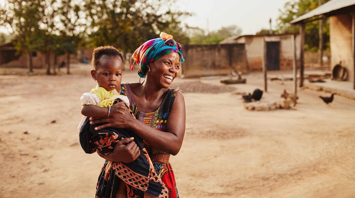 Ghana: Junge, lächelnde Frau hält Kleinkind im Arm.