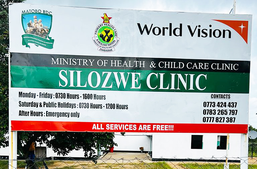 Simbabwe: eine grosse Tafel vor der Silozwe-Klinik mit den Öffnungszeiten und Telefonnummern. World Vision ist als Unterstützer aufgeführt.