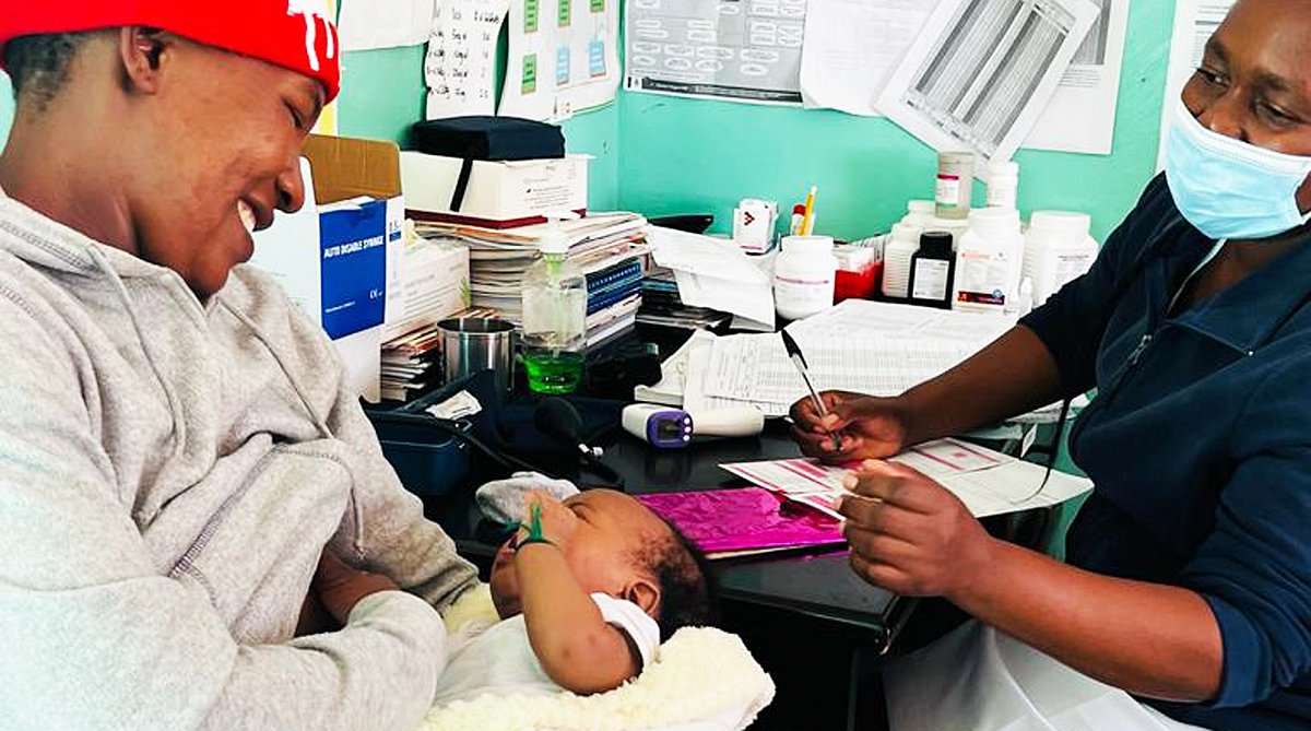 Simbabwe: Eine Frau hält im Behandlungsraum der Klinik ihr Baby auf dem Schoss. Eine Fachfrau Gesundheit widmet sich den beiden.
