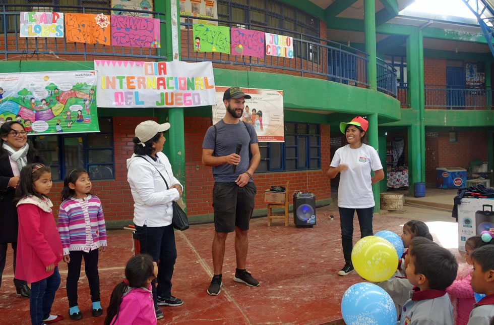 Bolivien: Ein Mann mit Mikrophon hält eine Rede vor einer Schar Kinder. Hinter ihm hängen bunte Plakate.