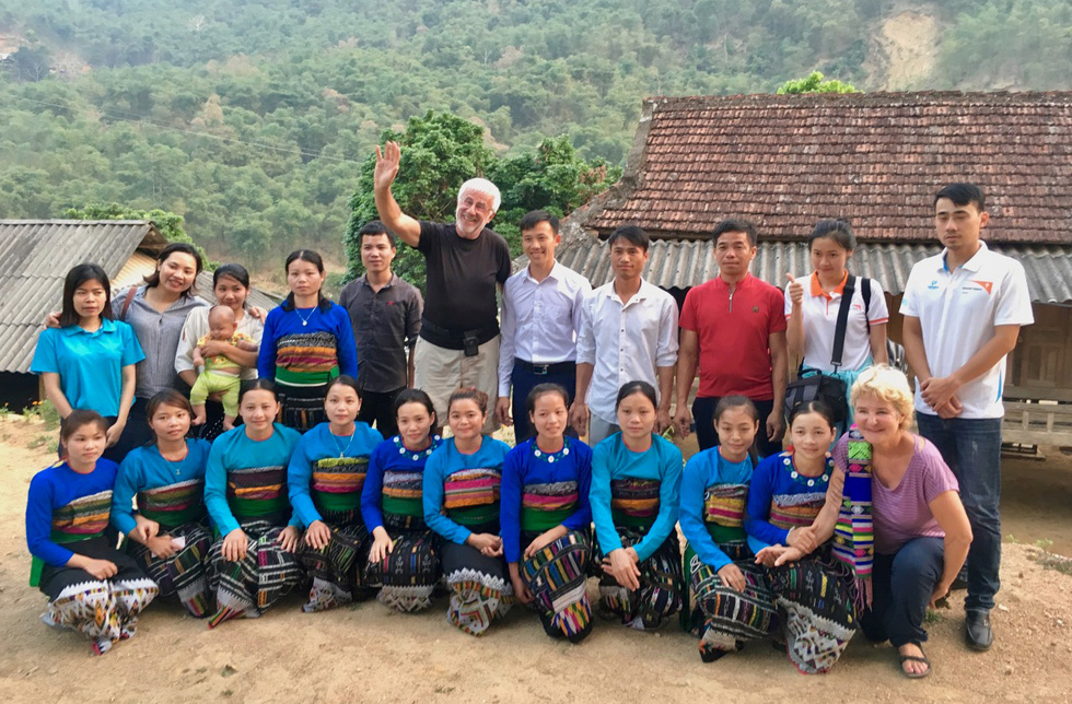 Vietnam: Gruppenbild mit Frauen in traditionellen, blauen Gewändern und europäischen Besuchern vor einem Dorf 