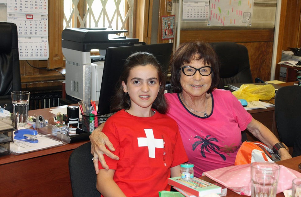 Georgien: Ein Mädchen im roten T-Shirt mit Schweizer Kreuz und eine Frau sitzen zusammen an einem Tisch.