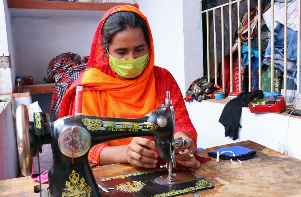 Eine Frau in Bangladesch sitzt an ihrer Nähmaschine und näht Masken.