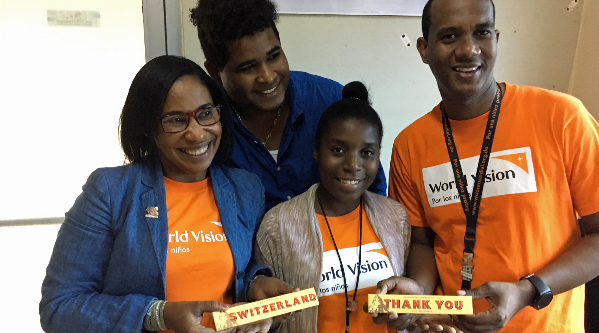 Dominikanische Republik: 4 lachende junge Menschen mit World-Vision-T-Shirts und Toblerone-Schokolade