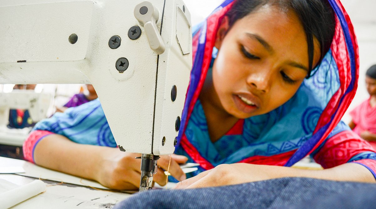 Bangladesch: Ein junges Mädchen arbeitet an einer weissen Nähmaschine. Sie trägt ein buntes Tuch und ein buntes Kleid.