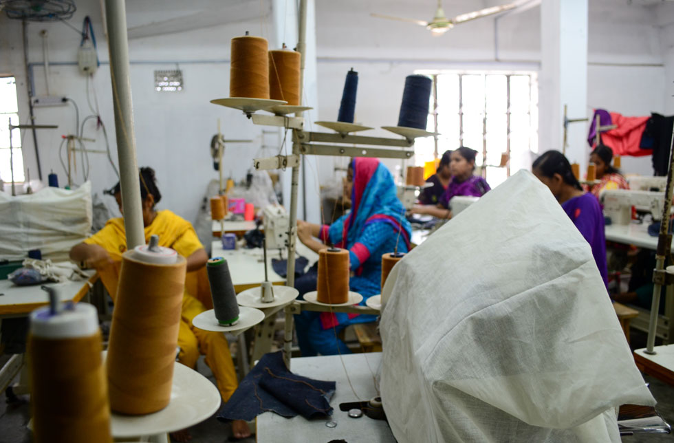 Bangladesch: Blick in eine Kleiderfabrik in Bangladesch mit einem Gewimmel an Nähmaschinen, Fäden, Schneiderinnen und Stoffen.