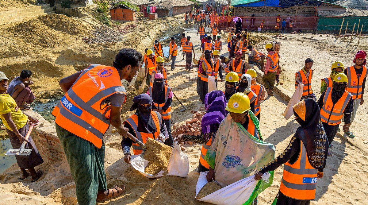 Cox’ Bazar, Bangladesch: Ein Gruppe Bauarbeiter in orangenen Gillets schaufeln Sand in Säcke.