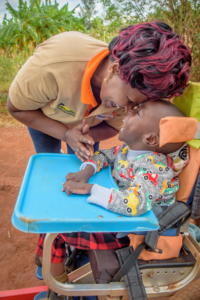 Kenia: Eine Betreuerin lacht gemeinsam mit einem Kind, das in einem Rollstuhl ist.