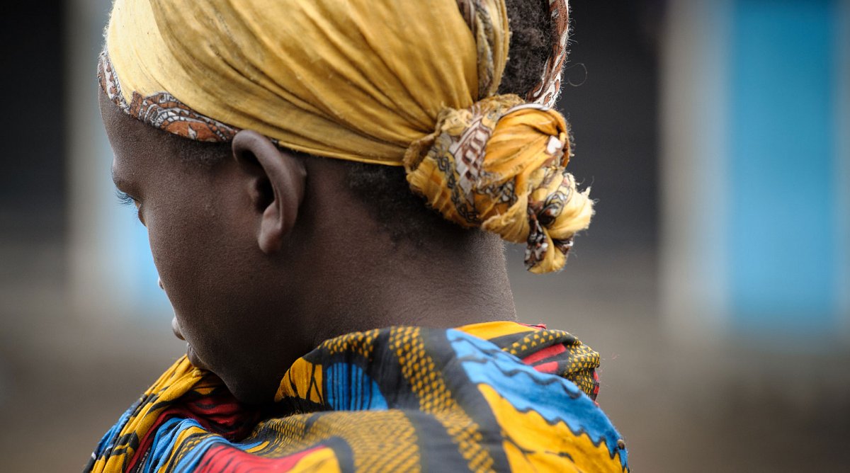 DRC/DRK: Ein Mädchen mit gelbem Kopftuch blickt weg von der Kamera. Sie trägt ein buntes Kleid.