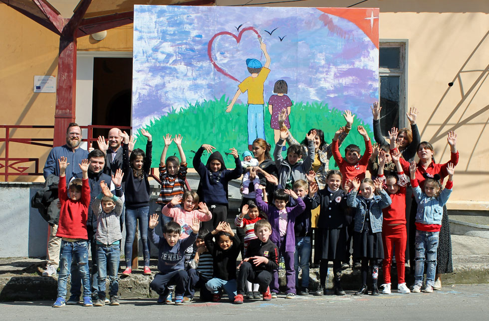Georgien: Eine Gruppe Kinder und Erwachsene posiert freudig vor einem selbstgemalten Plakat von World Vision.