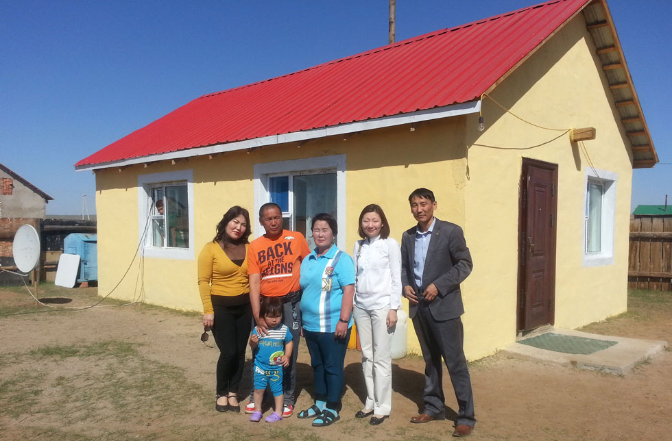 Mongolei: Eine Familie steht vor einem neu gebauten Haus.