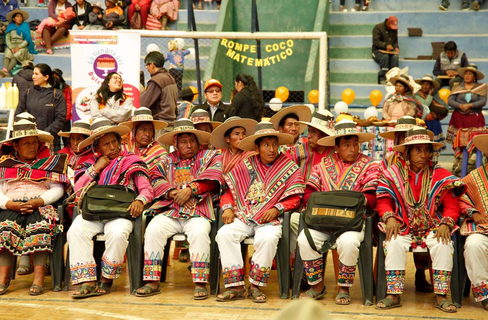 Bolivien: Eine Reihe von Männern in traditionellen Ponchos und Hosen sitzt in einem Stadion.