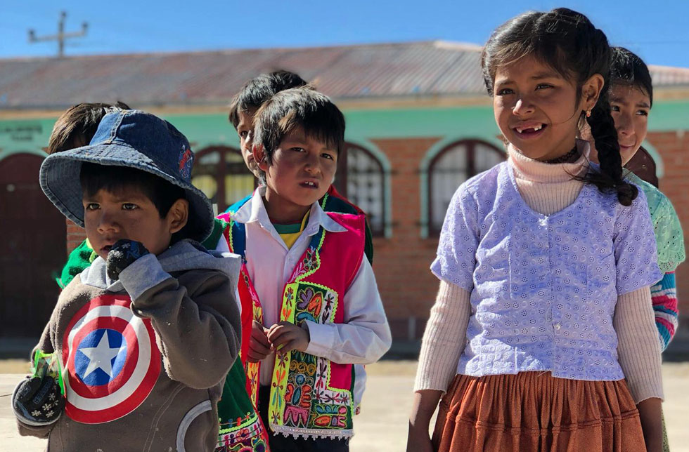 Bolivien: Ein kleines lachendes Mädchen mit Zahnlücke im Gesicht umgeben von lachenden Bubengesichtern.