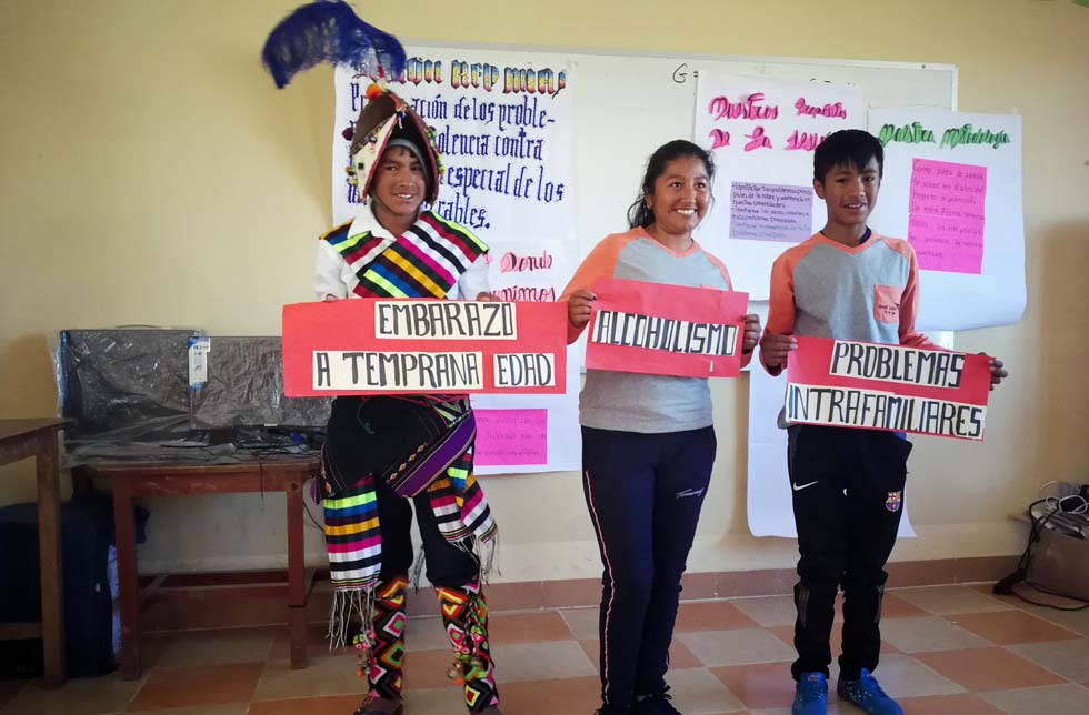 Bolivien: 2 Jungendliche und ein junges Mädchen halten Plakat mit der Aufschrift «Frühschwangerschaft», «Alkoholismus, und «familiäre Schwierigkeiten».