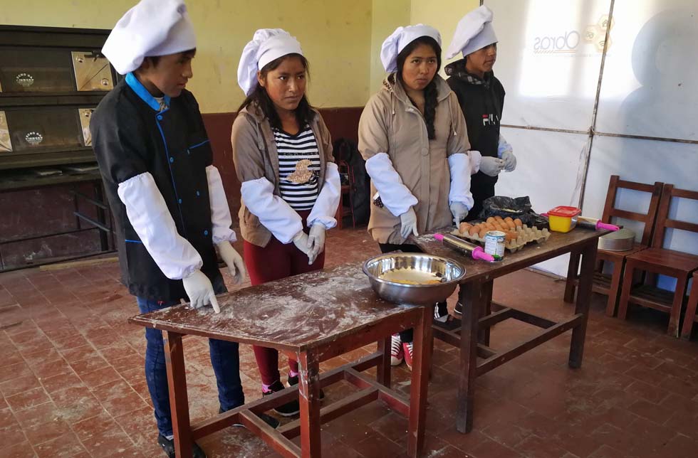 Bolivien: Zwei junge Frauen und zwei junge Männer mit Bäckermützen und handschuhen backen einen Kuchen.