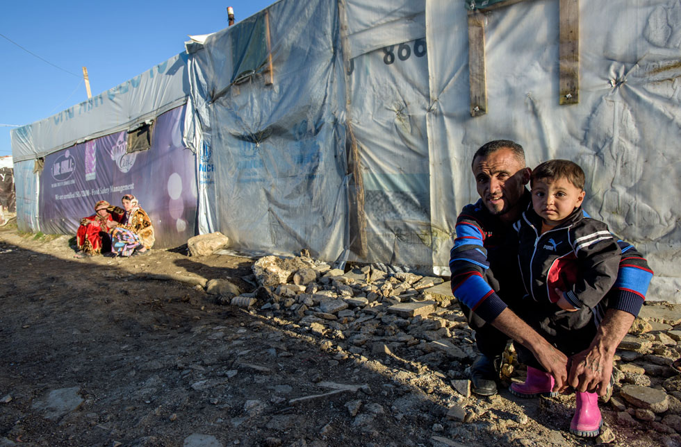 Syrien/Libanon: Eine Familie steht kniend vor den Zelten eines Flüchtlingslagers.