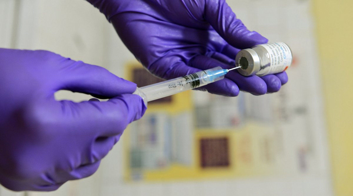 Eine Impfspritze wird von einer Person mit violetten Handschuhen aufgezogen.