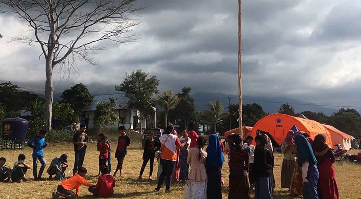 Indonesien, Menschen vor Notunterkünften mit Regenwolken
